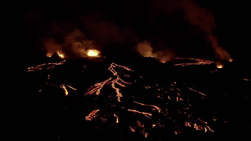 Lava erupting in crater and flowing down volcano slope contrasts with surrounding darkness at night