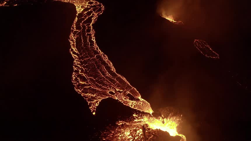 Molten hot lava glows in the darkness and splashes into the air as it flows from an erupting volcano