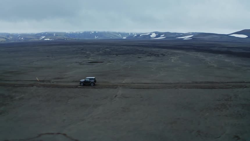A car travels on a dirt road in the desert with snowcapped mountains in the distance