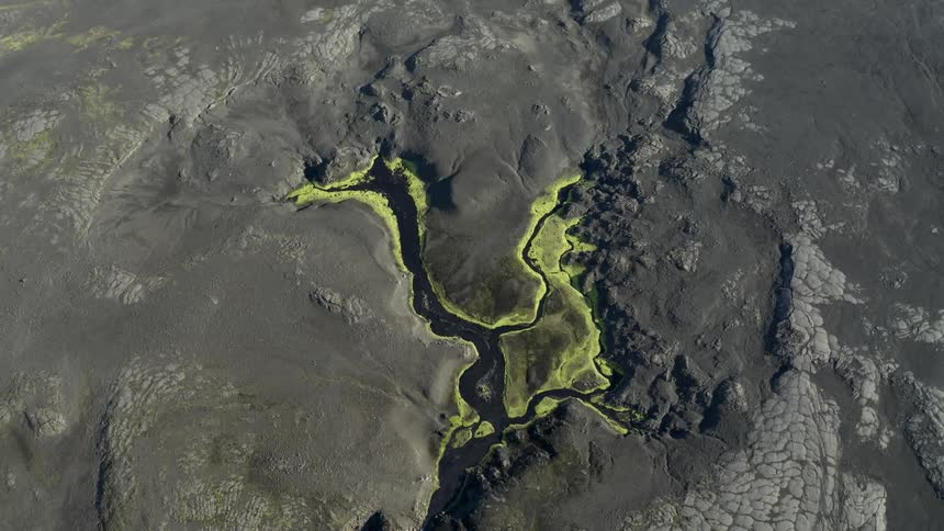 Aerial of river surrounded by bright yellow stained ground flowing through dull gray terrain
