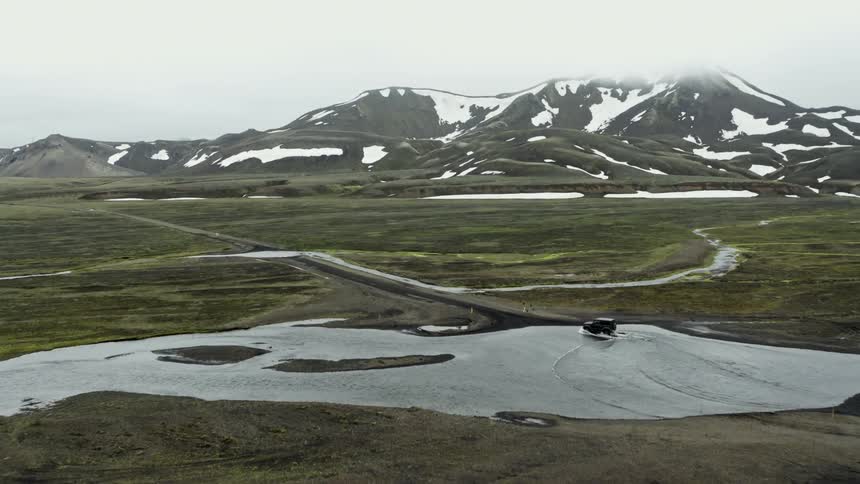 A sport utility vehicle drives across a shallow river in a remote mountainous area
