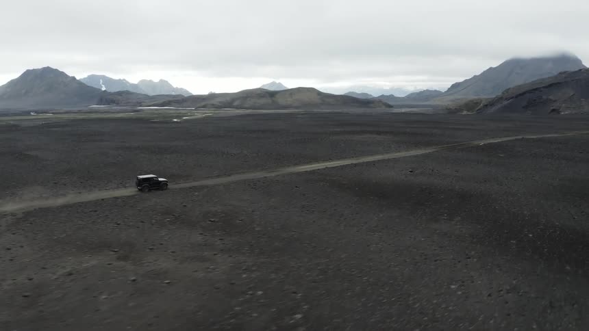 A black jeep travels on a rural road among mountains