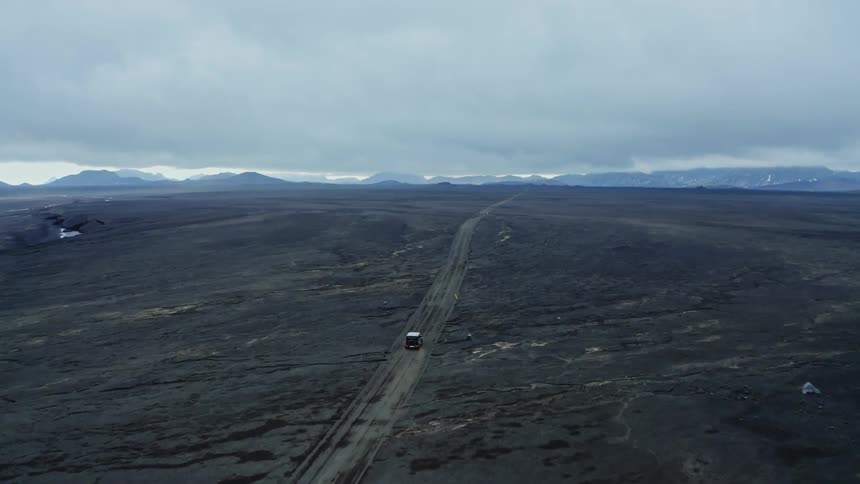 Car traveling on a dirt road leading to the mountains in the distance