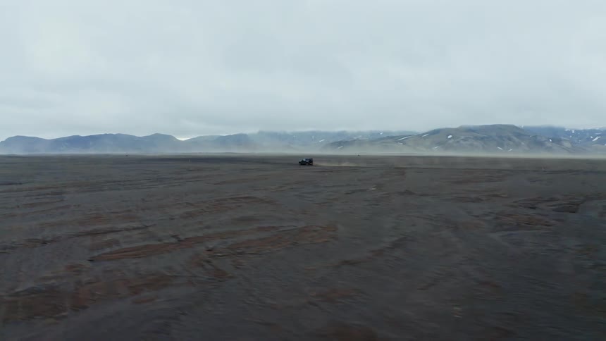 Jeep speeding across the sandy expanse with mountains in the background