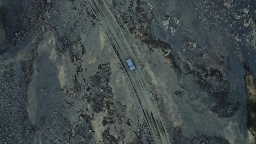 Aerial view of a blue car driving on a desert road