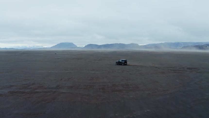 Vehicle drives across plain bordered by misty mountains on an overcast day