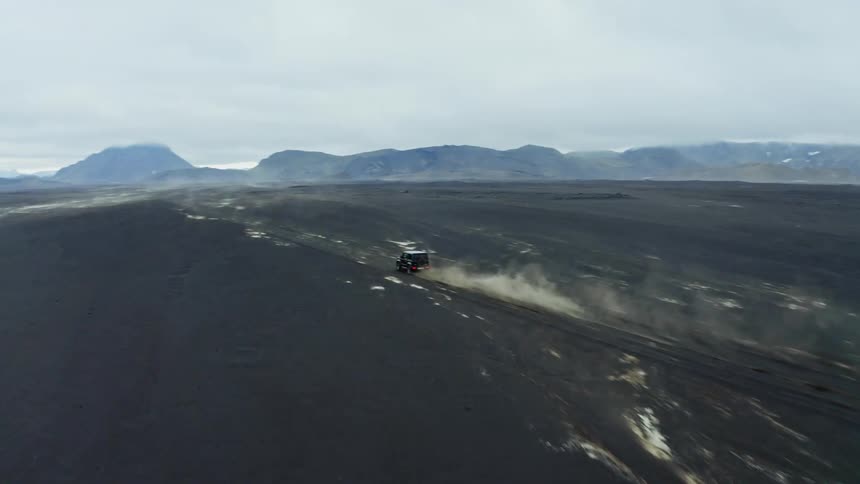 Vehicle drives across dirt landscape mountains on horizon