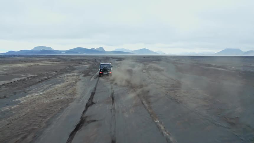 A sport utility vehicle drives across barren land on a cloudy day