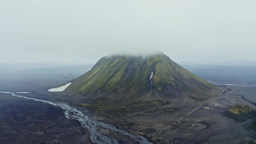 Aerial landscape of a mountain with the peak covered by mist surrounded by flat areas and streams during day time
