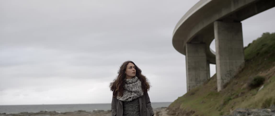 A woman stands by a bridge on a cloudy day