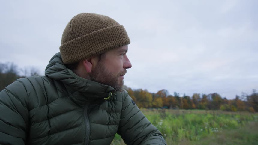 Man wearing beanie and puffer jacket outside near trees in fall color
