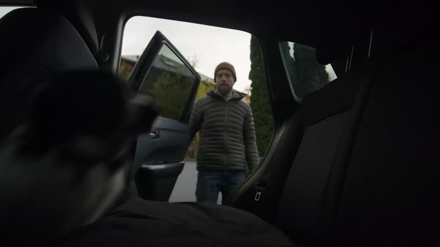 A man opens the door of his suv and his dog jumps in and climbs onto the seat and the man closes the door