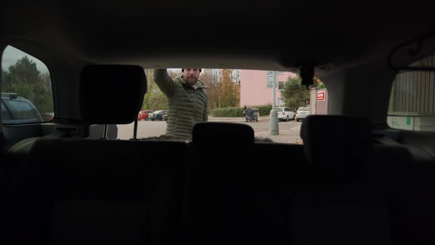 A man opens the trunk of his car and looks at the dog then closes it