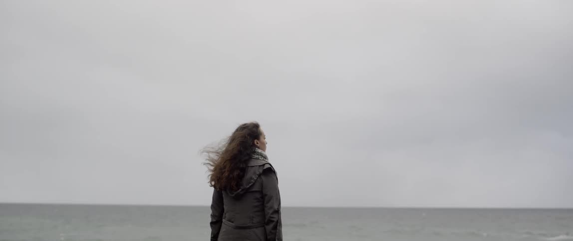 A woman stands near the water on a windy day