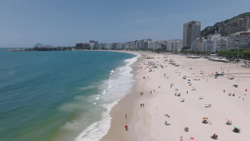 Waves roll onto busy beach bordering hotels at the base of mountains