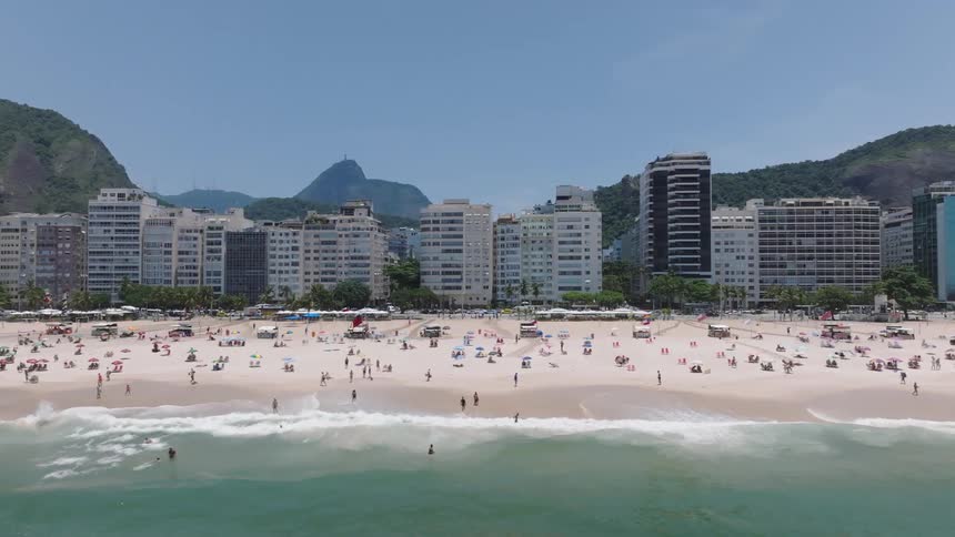 Crowd of people at a beach with the ocean to one side and an urban area to the other during day time