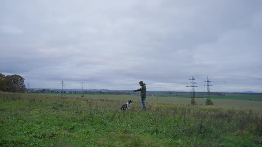 A man plays with his dog in a rural grassy field on an autumn day