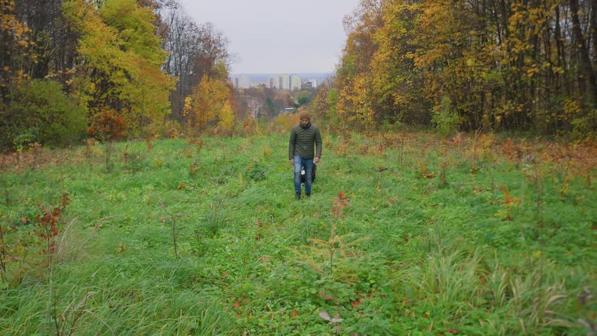 Man walking with his dog through the vegetation with a view of buildings from city in the background