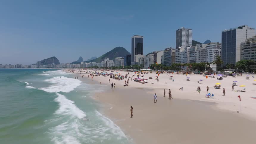 A crowd of people are walking and relaxing on the beach in a tourist area on a sunny day