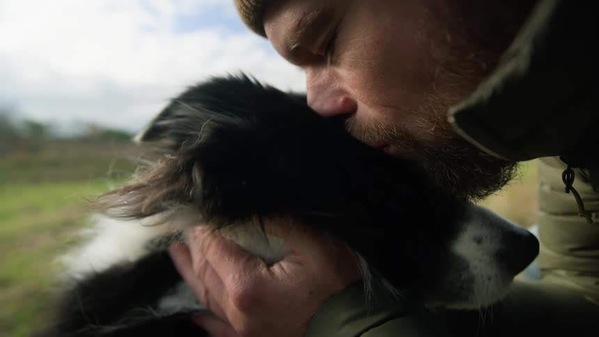 Man squatting kisses and fondles a border collie dog during day time
