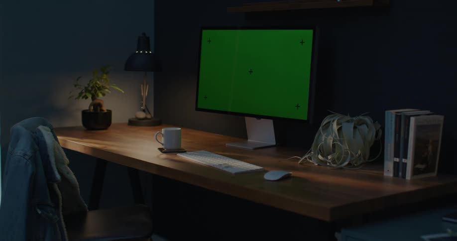 A home office workspace at night as headlights from a car shine onto the desk and computer monitor
