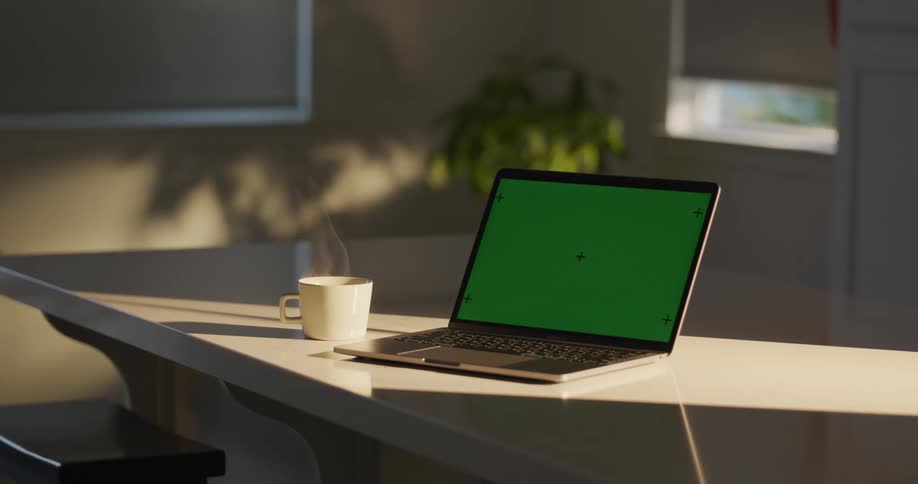 A laptop computer with a green screen on a table as steam rises from a cup of coffee
