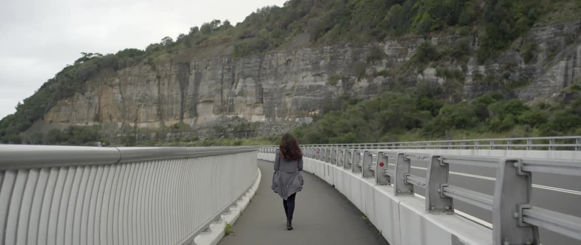 A woman in a gray jacket walks near a highway