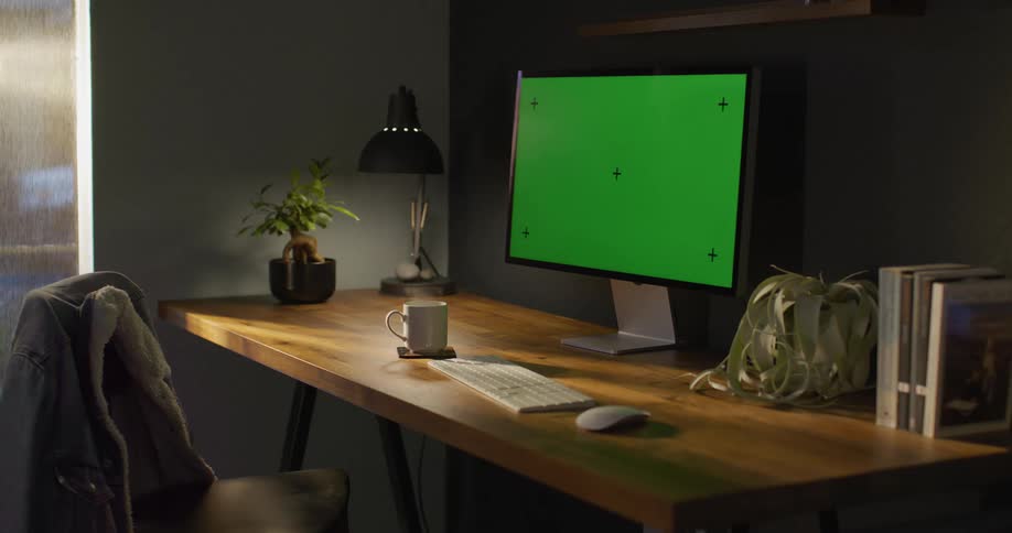 Steam rises from a cup of coffee on a table in front of a computer with a green screen
