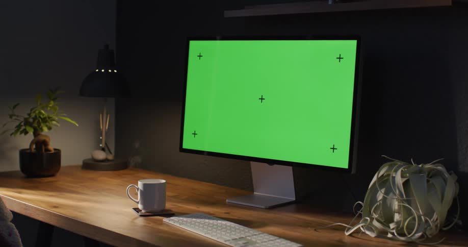 A computer monitor sits on a wooden desk next to a steaming cup of coffee