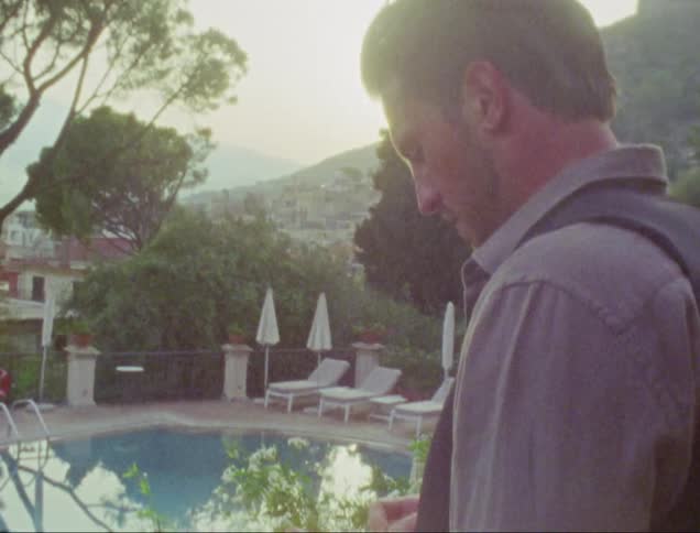 Man on a balcony taking notes of swimming area at hotel overlooking coast
