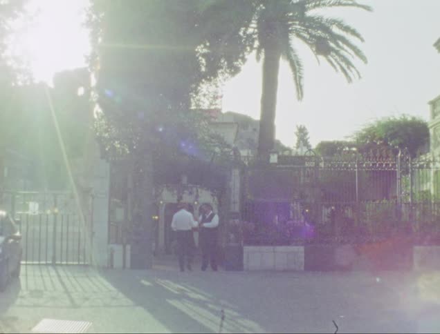 Man walks to the entrance of a house and is greeted by a friend before entering caught on vintage film