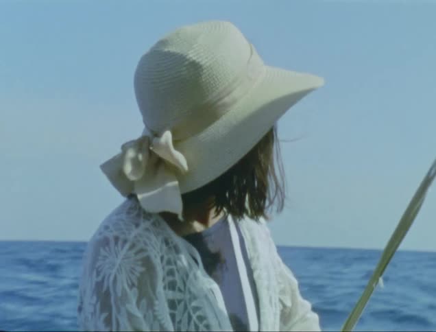Woman with white hat and shirt travels on sailboat watching sea