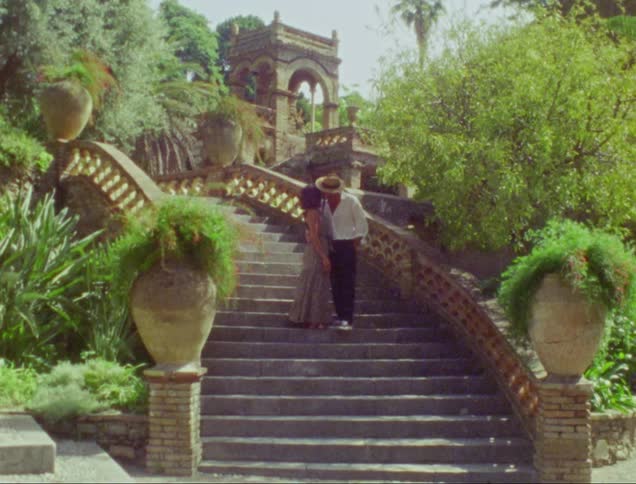 Young couple kiss while standing on a tropical mansion staircase on the garden caught on vintage film