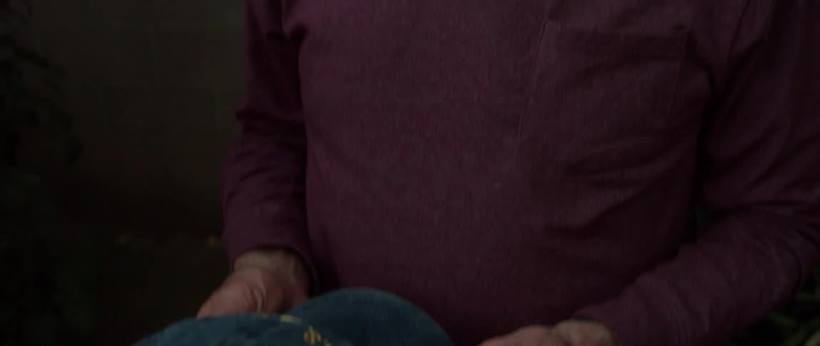 Elderly man sitting in his backyard and holding his cap sentimentally