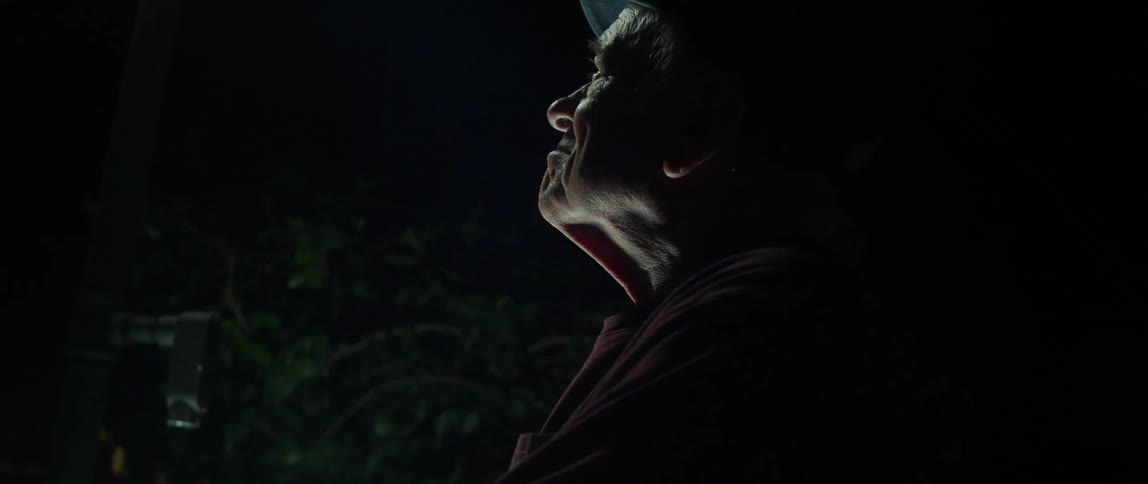 Closeup of an elderly person outdoors at night looking upwards with a thoughtful gaze