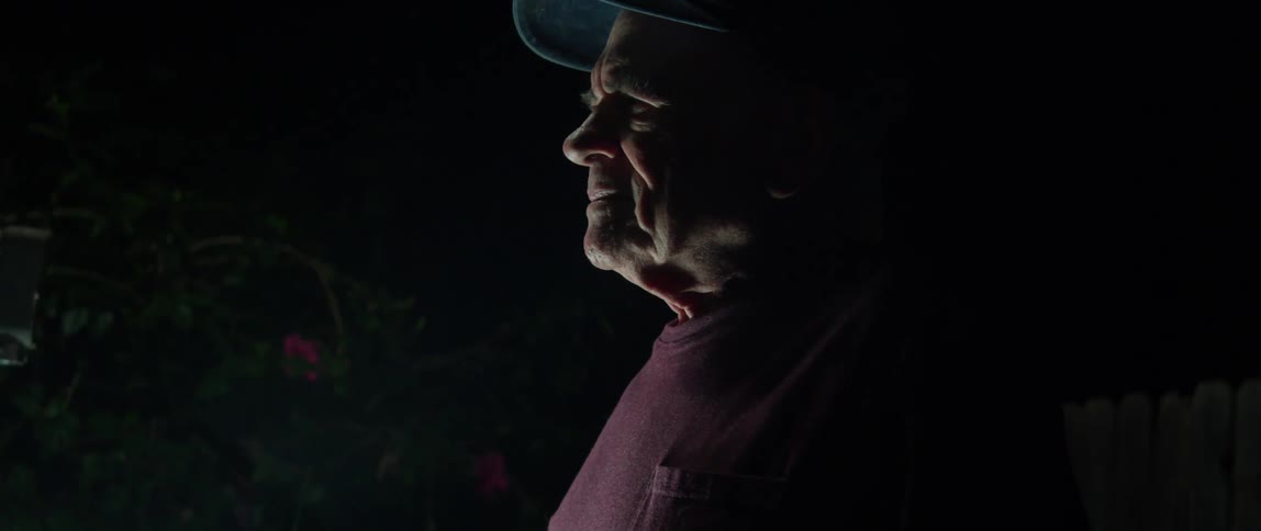 Elderly person wearing a hat outdoors at night looking upwards