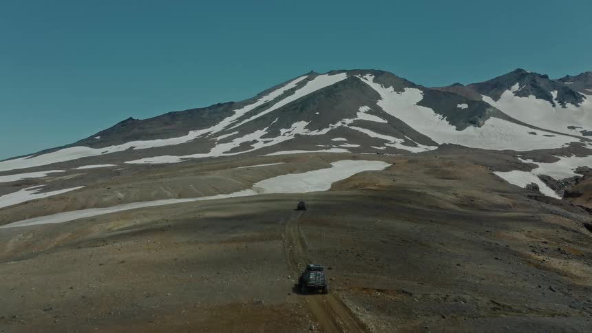 Aerial panorama of jeeps driving on the ground in snowy mountains