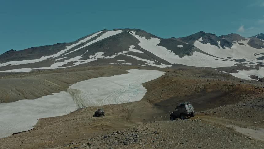 Aerial panorama of two cars driving on the ground with mountains of snow in front of them