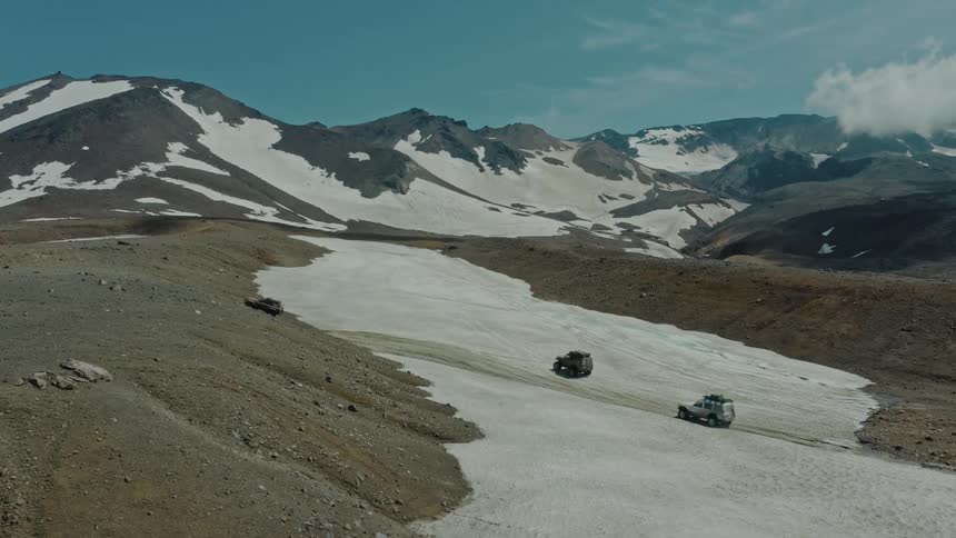 Aerial panorama of three jeeps driving on the ground in snowy mountains