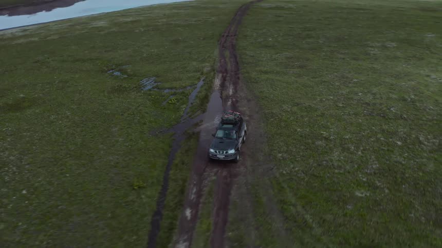 Car drives on a dirt road filled with water and mud near icy water