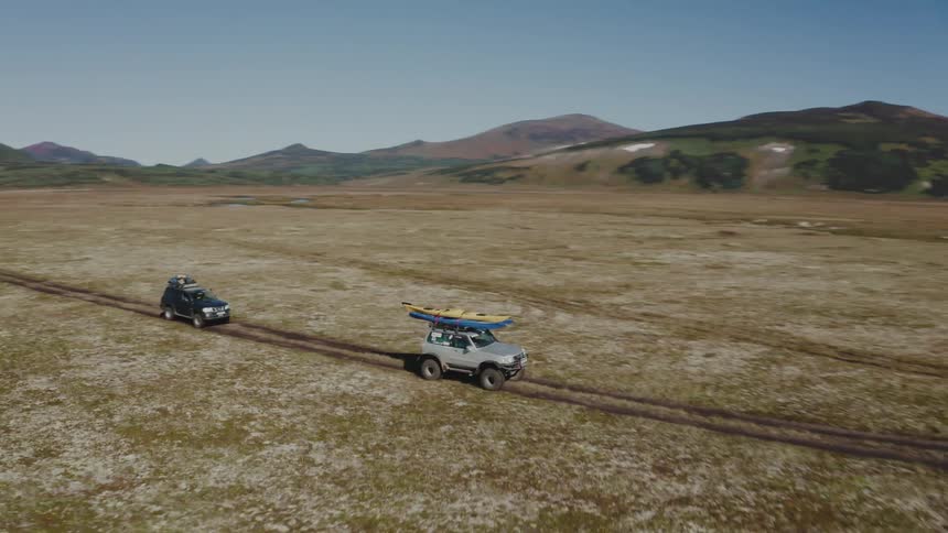 Two jeeps driving through nature in fields surrounded by mountains in the daylight