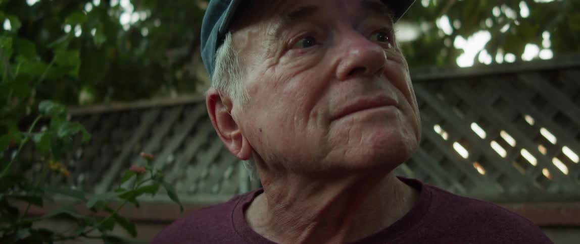 Elderly man wearing a baseball cap in the backyard