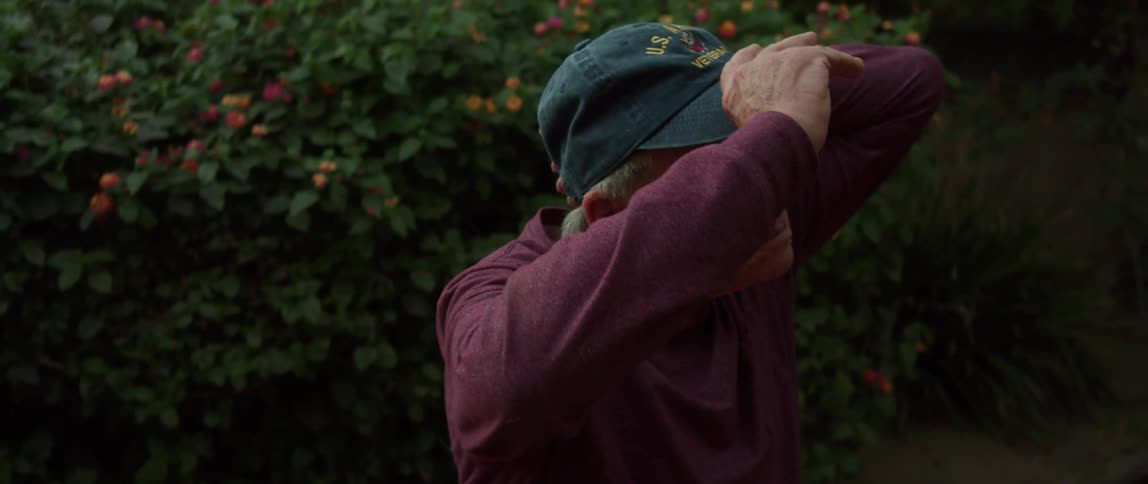 Elderly person in the backyard and garden putting on a cap while thoughtfully looking upwards