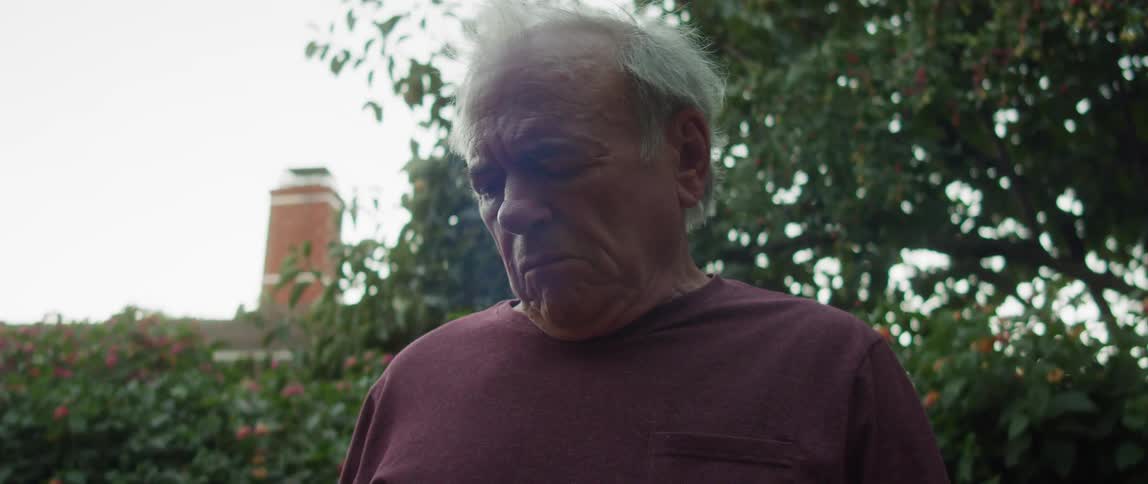 Elderly person in a garden looking at their cap in their hands with a facial expression of emotion
