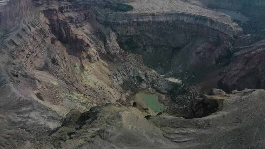 Aerial panorama of a crater with a blue lake amidst the mountains in the daylight
