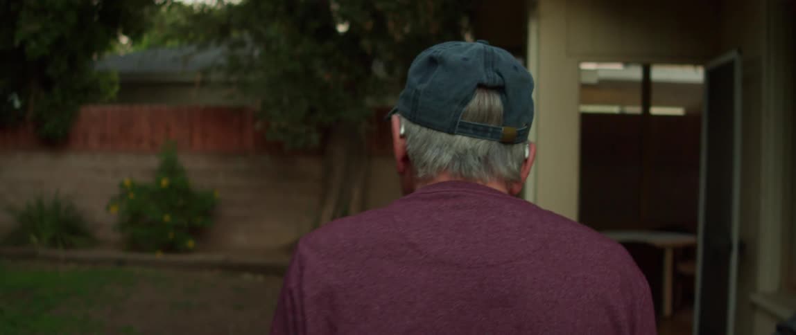 Elderly person with a cap walking in the backyard of their house