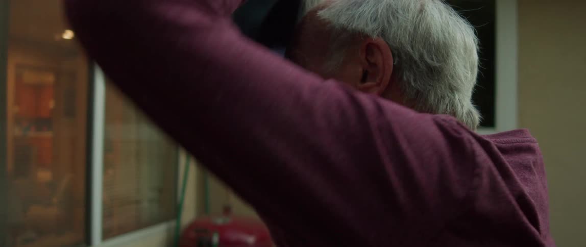 Elderly man standing in the backyard puts on a baseball cap