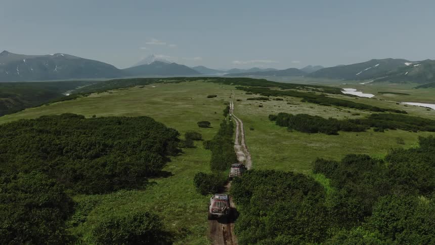 Two jeeps driving on a dirt road through a grassland with mountains on the horizon in the daylight