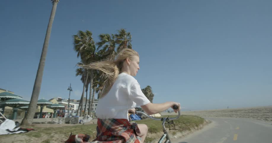 A girl rides a bicycle on a path near the beach