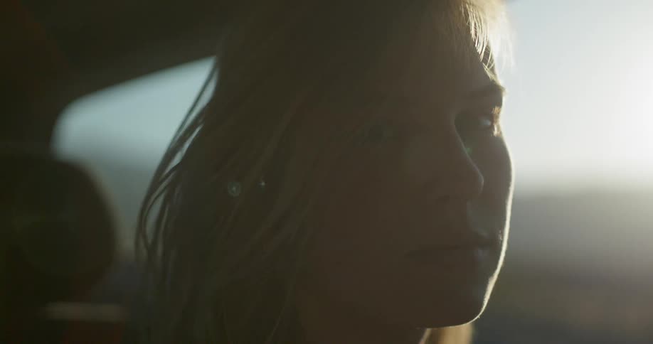 A woman sits in a car as wind blows her hair